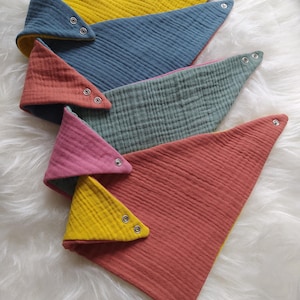 May include: Four triangular fabric bibs with snap closures. The bibs are reversible and feature a variety of colors, including yellow, blue, green, and red.