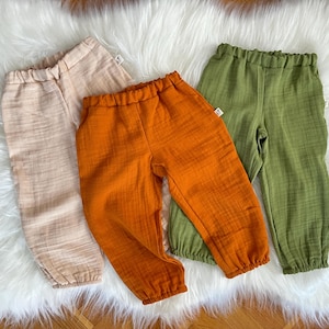 May include: Three pairs of cotton pants in different colors: beige, orange, and green. The pants have a relaxed fit and a drawstring waistband.
