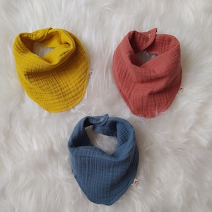 Pode incluir: Três babadores de algodão para bebé em amarelo, vermelho e azul. Os babadores são feitos de um tecido macio e texturizado e têm uma forma triangular.