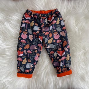 May include: Black and navy blue leggings with an orange waistband. The leggings feature a repeating pattern of owls, foxes, hedgehogs, and mushrooms.