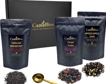 May include: A black gift box labeled Camellios Finest Tea Collection with three black pouches of English Breakfast, Forest Fruits, and Spiced Apple Chai tea. Three piles of loose tea leaves are arranged with a gold-toned metal tea measuring spoon.
