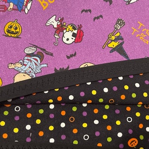 May include: Close-up of Halloween-themed fabric featuring Snoopy and the Peanuts gang in costumes. The purple fabric has pumpkins and bats. Below is black fabric with white, orange, and purple polka dots. A black zigzag trim separates the fabrics.