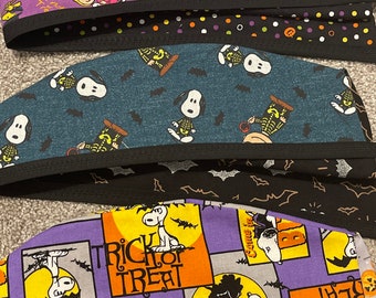 Könnte beinhalten: Mehrere OP-Hauben zum Thema Halloween mit Snoopy und der Peanuts-Gang. Die Hauben haben einen schwarzen Rand und sind mit Kürbissen, Fledermäusen und den Worten "Trick or Treat" gemustert. Zu den Farben gehören Lila, Türkis und Schwarz.