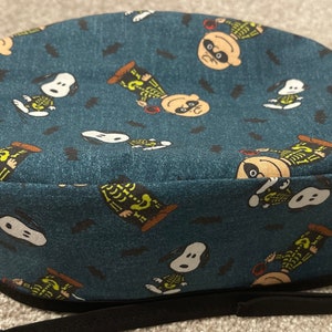 May include: A blue fabric cap featuring a repeating pattern of Snoopy and Charlie Brown dressed as skeletons, with black bat silhouettes. The cap has a black elastic band and is likely for medical or culinary use.
