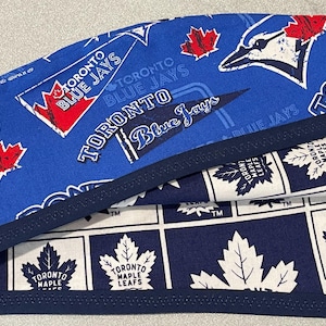 May include: Two fabric headbands. One is blue with Toronto Blue Jays logos and text. The other is navy blue and white with Toronto Maple Leafs logos and text. Both have a navy blue trim.