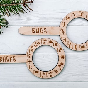 May include: Two wooden magnifying glass-shaped identification guides with handles. The top guide is labeled "BUGS" and features various insect silhouettes. The bottom guide is labeled "TRACKS" and features various animal footprints.