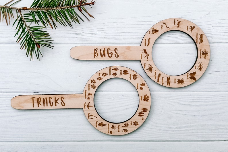 May include: Two wooden magnifying glass-shaped identification guides with handles. The top guide is labeled "BUGS" and features various insect silhouettes. The bottom guide is labeled "TRACKS" and features various animal footprints.