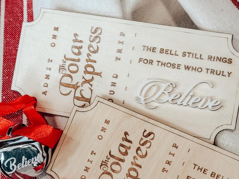 May include: Wooden Polar Express tickets with engraved text and a silver bell ornament with a red ribbon. The tickets read "Admit One" and "The Polar Express" with the phrase "The bell still rings for those who truly believe."