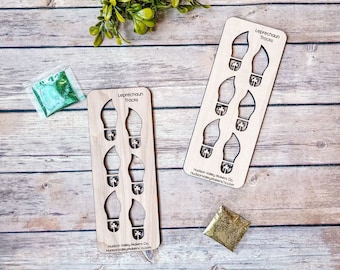 May include: Two wooden stencils with the words "Leprechaun Tracks" and the outline of four leprechaun footprints. Each footprint has a shamrock cut out. The stencils are on a wooden surface with green and gold glitter.