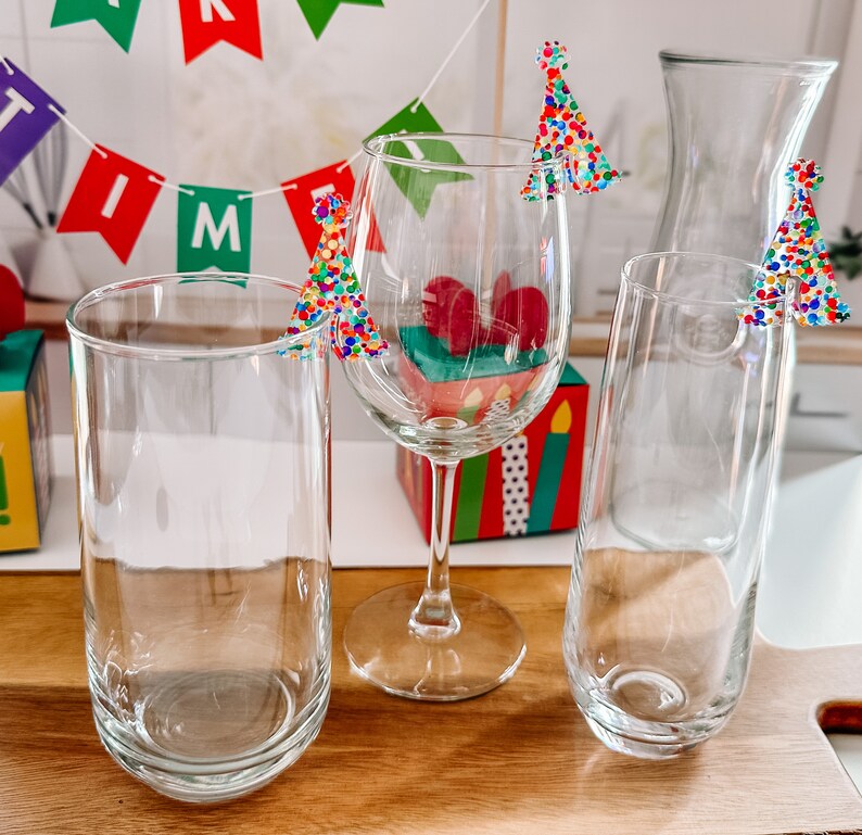 May include: Four clear glass drinking glasses with colorful, confetti-like Christmas tree toppers. The glasses are on a wooden surface.