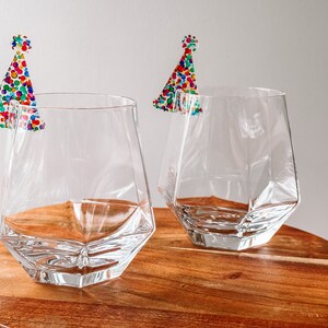 May include: Two clear glass tumblers with a geometric design, each with a colorful confetti party hat sticker on the rim.