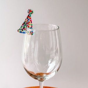 May include: A clear glass wine glass with a colorful confetti party hat on the rim.