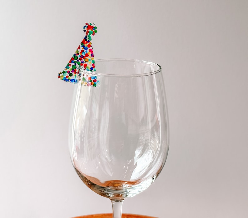 May include: A clear glass wine glass with a colorful confetti party hat on the rim.