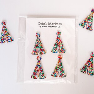 May include: Set of six colorful party hat drink markers. The markers are made of white acrylic and feature a confetti pattern. The markers are packaged in a clear plastic bag with a white card that reads "Drink Markers By Hudson Valley Makers Co."