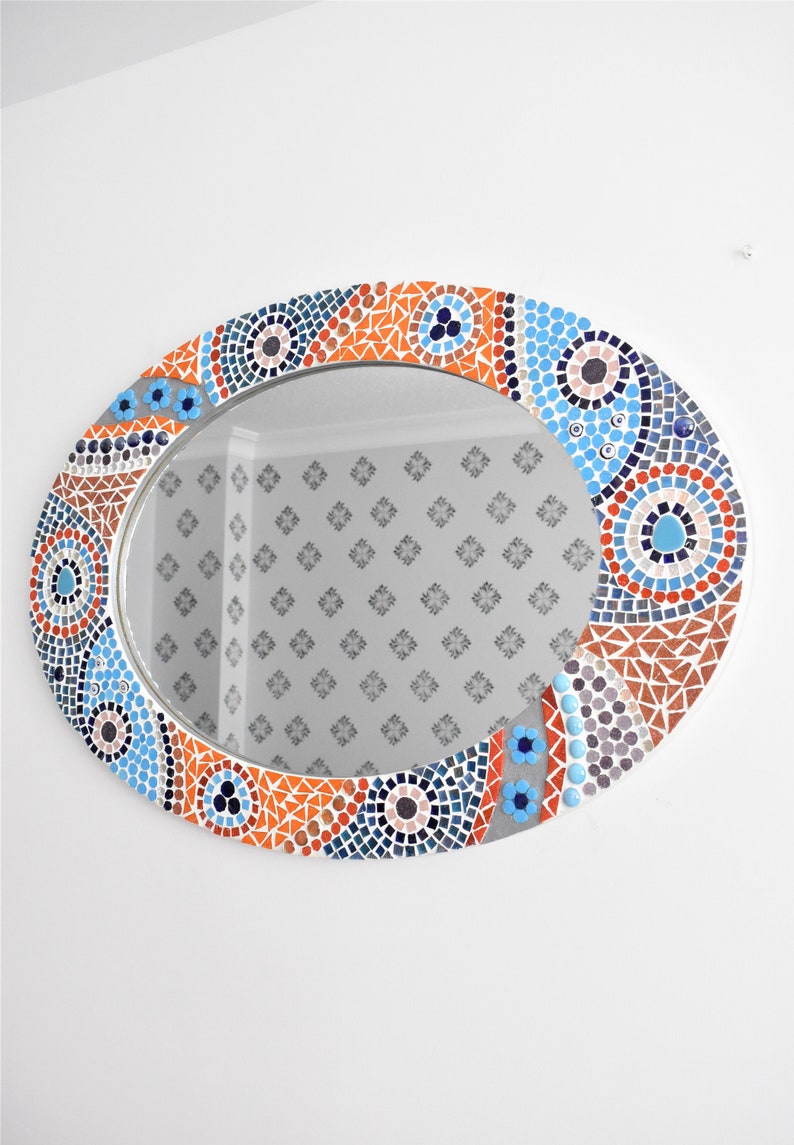 May include: Oval mirror with a mosaic frame in shades of blue, orange, and gray. The frame features geometric patterns and circular designs.