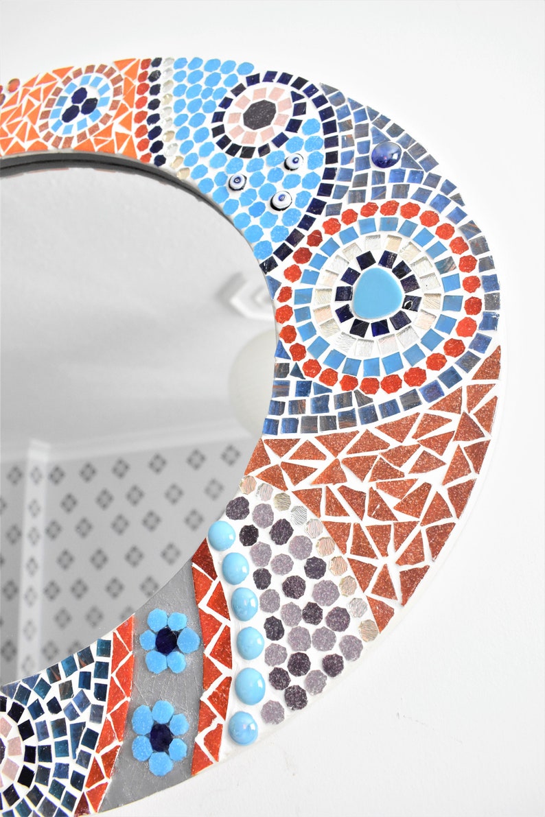May include: A round mirror with a mosaic design in shades of blue, red, orange, and white. The mosaic features geometric shapes and patterns, including circles, triangles, and squares.