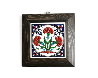 May include: A framed ceramic tile with a traditional Turkish design featuring three red carnations with green leaves and blue accents on a white background.