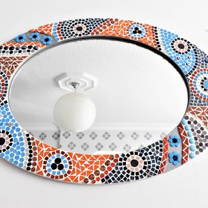 May include: Oval mirror with a mosaic frame in shades of blue, orange, black, and white. The frame features a geometric pattern with circles and triangles.