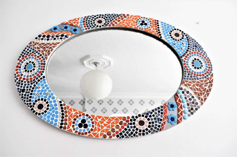 May include: Oval mirror with a mosaic frame in shades of blue, orange, black, and white. The frame features a geometric pattern with circles and triangles.