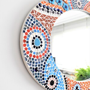 May include: Round mirror with a mosaic frame featuring blue, red, and orange tiles in a geometric pattern.