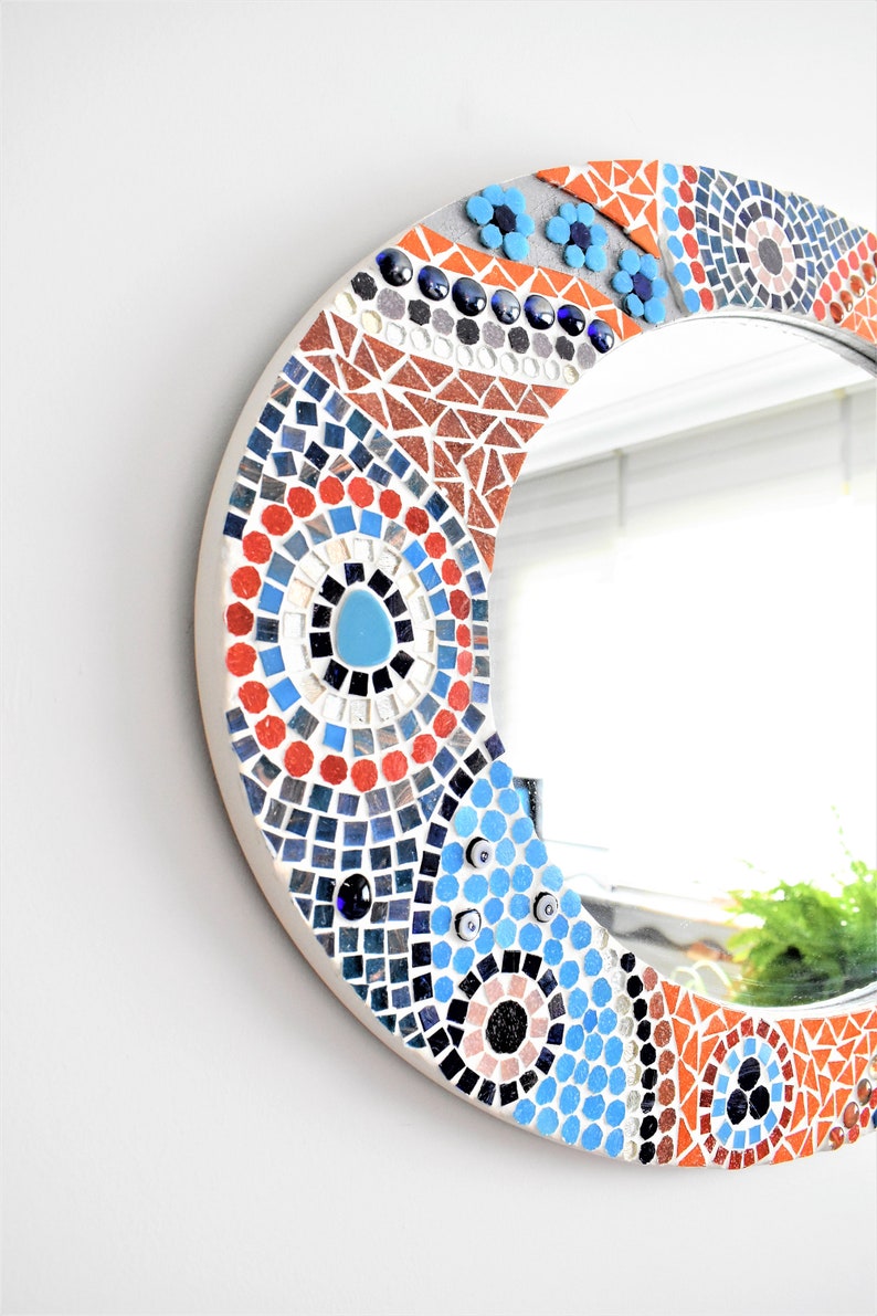 May include: Round mirror with a mosaic frame featuring blue, red, and orange tiles in a geometric pattern.