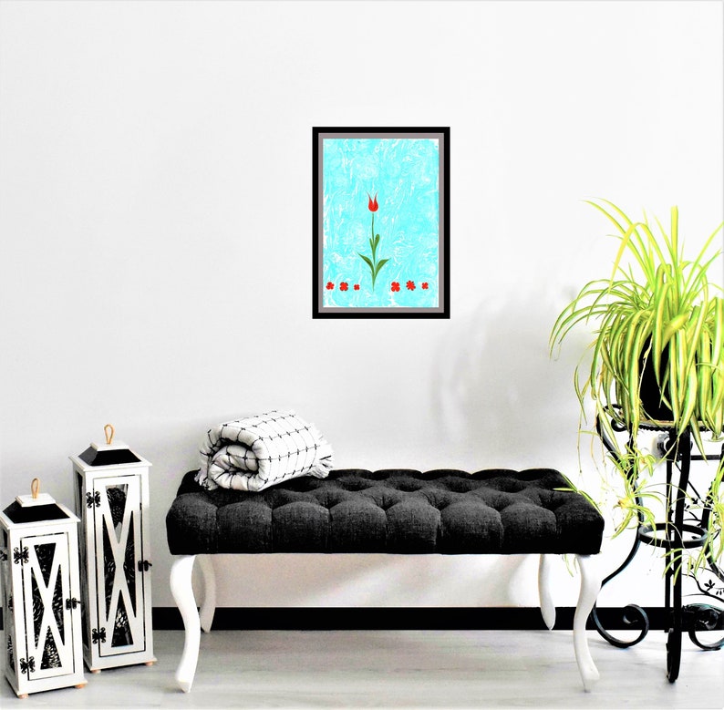 May include: A framed print of a red tulip with green leaves on a blue background. The print is hanging on a white wall above a black tufted bench.