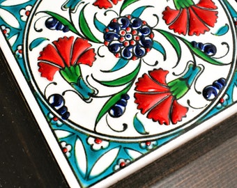 May include: A framed ceramic tile with a colorful floral design. The tile features red, blue, green, and white flowers with intricate details. The frame is dark brown wood.