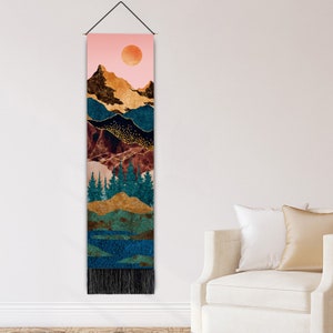 Puede incluir: Un tapiz de pared vertical con un dise&ntilde;o de paisaje. La obra de arte presenta un cielo rosa con un sol naranja, monta&ntilde;as en oro y verde azulado, y un bosque de &aacute;rboles verde azulado. La parte inferior tiene un &aacute;rea texturizada azul y verde y una franja negra.
