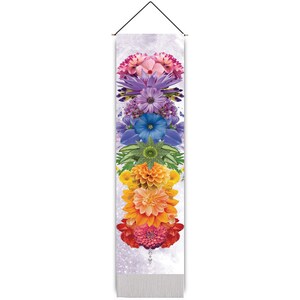 May include: A colorful wall tapestry featuring a rainbow of flowers arranged in a vertical stack. The flowers are arranged in the order of the chakras, starting with the root chakra at the bottom and ending with the crown chakra at the top. The tapestry is made of a soft, woven fabric and has a fringed edge.