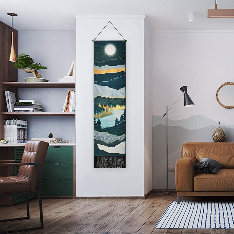 May include: A tapestry wall hanging with a dark blue, green, and gold mountain landscape design. The tapestry features a full moon and a lake with trees. The tapestry has a fringe border.