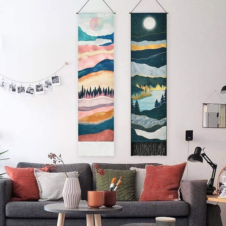 May include: Two colorful tapestry wall hangings with mountain and lake scenes. The left tapestry features a pink, orange, and blue mountain scene with a white moon. The right tapestry features a blue and green mountain scene with a lake and a white moon.
