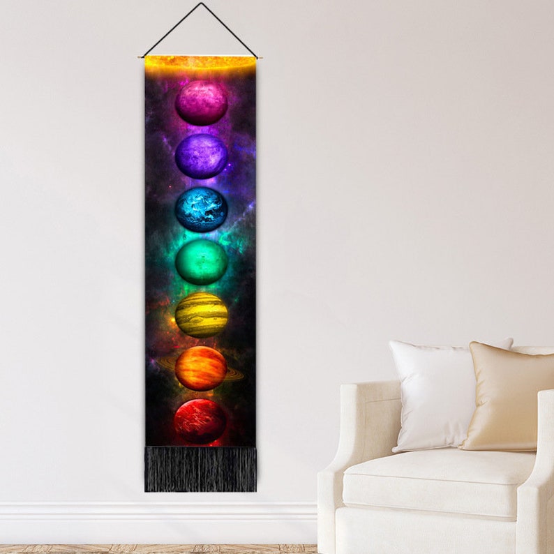 May include: A tapestry with a black background and a vertical row of seven colorful planets. The planets are arranged in a rainbow pattern, with the top planet being red and the bottom planet being purple. The tapestry has a fringe border.