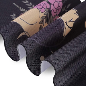 May include: Black fabric with a floral pattern in shades of pink and beige. The fabric has a textured surface and is folded over on itself.