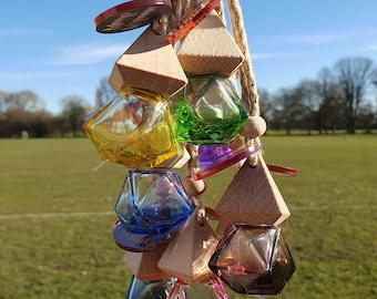 May include: A hanging decorative mobile featuring wooden geometric shapes and colorful glass prisms. The prisms are in various colors, including yellow, green, blue, and red. The mobile is suspended from a natural rope, creating a visually appealing display.
