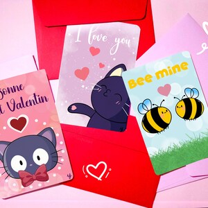 Può includere: Quattro biglietti di San Valentino con diversi design che presentano simpatici animali dei cartoni animati. I biglietti sono rosa, blu e gialli con pois bianchi e cuori. Il testo sui biglietti recita "Bonne Saint Valentin", "Ti amo", "Sii mio", e un cuore.