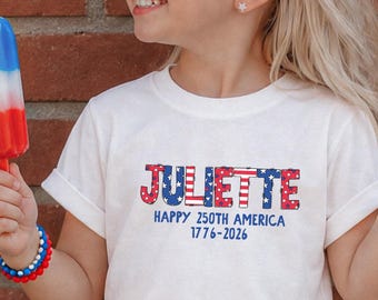 May include: A white t-shirt featuring the name JULIETTE in a red, white, and blue American flag pattern, with the text HAPPY 250TH AMERICA 1776-2026 printed below in blue. The shirt is paired with blue denim shorts featuring a white star and red stripe pattern.