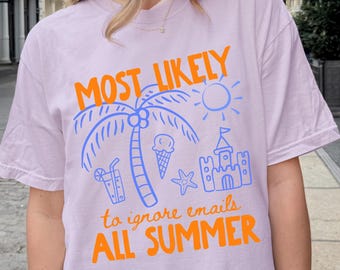 May include: A light purple t-shirt with the text "MOST LIKELY to ignore emails ALL SUMMER" in orange and blue. The shirt features a palm tree, sun, ice cream cone, starfish, and sandcastle graphic.