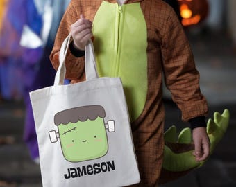 May include: A white canvas tote bag featuring a cartoon illustration of a green Frankenstein-style monster head with a dark grey hair top, bolts on the sides, and pink cheeks. The name Jameson is printed in black capital letters below the graphic.