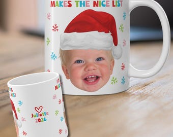 May include: Two white ceramic mugs featuring a photo of a smiling child wearing a red Santa hat. The text reads MY LALA ALWAYS MAKES THE NICE LIST and JULIETTE 2026 with a red heart. The design includes colorful snowflake patterns in red, green, and blue.