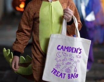 May include: A white canvas tote bag featuring purple text that reads CAMDEN'S TREAT BAG, surrounded by various Halloween-themed icons including a crescent moon, bat, spider, witch hat, candy corn, ghost, spiderweb, lightning bolt, and pumpkin.