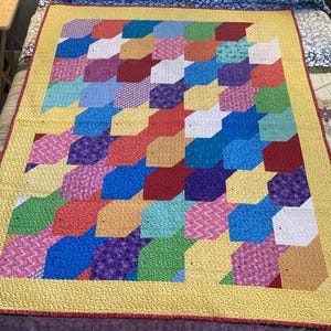 May include: A colorful quilt with a geometric pattern of hexagons in shades of red, blue, yellow, green, purple, and white. The quilt is made with a variety of fabrics, including floral prints, geometric patterns, and solid colors.