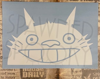 May include: A white vinyl decal of Totoro's smiling face from the animated film My Neighbour Totoro. The decal is on a light blue background. The text "Spawned Story" is faintly visible.