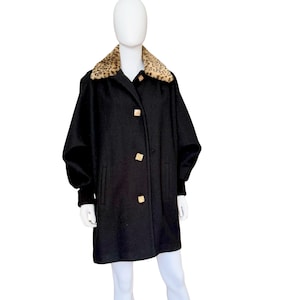 May include: A black coat with a leopard print collar and gold-colored square buttons. The coat has a classic design with a slightly oversized fit and long sleeves. The coat is displayed on a mannequin.