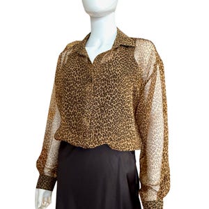 May include: A leopard print blouse with long sleeves and a collared neckline. The blouse features a brown and black animal print pattern. The sleeves are sheer, and the blouse is paired with a black skirt.