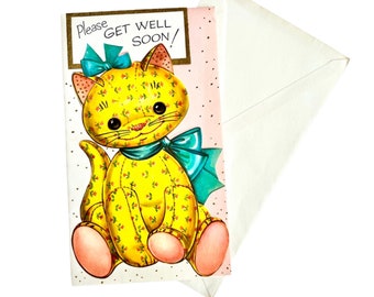 May include: A yellow cat with a blue bow and floral print, sitting on a pink and white card with the text "Please Get Well Soon!"