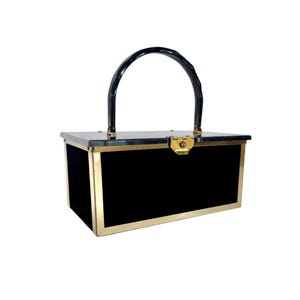 May include: A vintage black handbag with a rectangular shape, featuring a black handle and gold-colored trim. The bag has a gold clasp closure and a black velvet exterior.