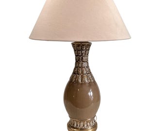 May include: A brown ceramic table lamp with a white fabric lampshade. The lamp base has a textured design and a gold base.