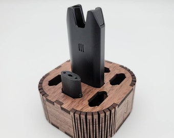 May include: A wooden stand with a black vape pen and a smaller black vape cartridge. The stand is made of dark wood and has a decorative design.