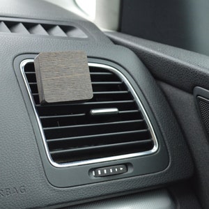 Könnte beinhalten: Ein dunkler Holz-Lufterfrischer für die Lüftung eines Autos. Der Clip ist an einer schwarzen Lüftung im Auto befestigt.