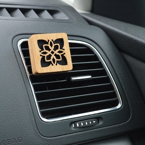 Op de afbeelding: Een houten autoluchtverfrisser met een geometrisch ontwerp. De luchtverfrisser is bevestigd aan een ventilatieopening in een auto.